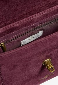 Borsa in suede di un profondo bordeaux con una texture morbida. Presenta una tasca con zip, hardware metallico e un'etichetta con la scritta "LOVE & ROSES."