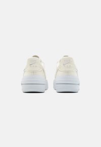 Bílé kožené tenisky s polstrovanými límci a texturovanými gumovými podrážkami. Na patě a na boku se nachází šedé logo "Nike Air".