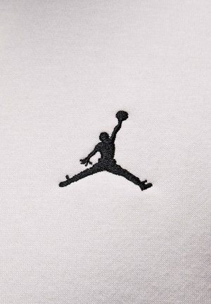 Black embroidered Jumpman logo on a white, textured fabric background, with a smooth, cotton-like appearance.