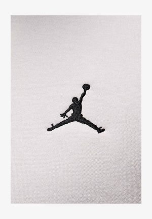 Logo Jumpman ricamato in nero su uno sfondo di tessuto bianco e testurizzato, con un aspetto morbido simile al cotone.