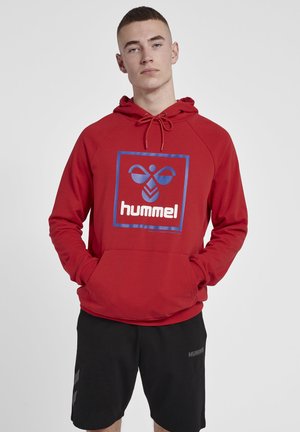 Rode hoodie met een blauwe vierkante graphic waarop het merk "hummel" in witte tekst staat. Voorzien van een capuchon met trekkoord en een voorzak.
