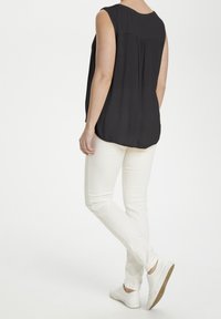 Haut noir sans manches avec un ourlet arrondi, associé à un jean blanc ajusté et des baskets blanches. Le haut présente un détail plissé subtil à l'arrière.