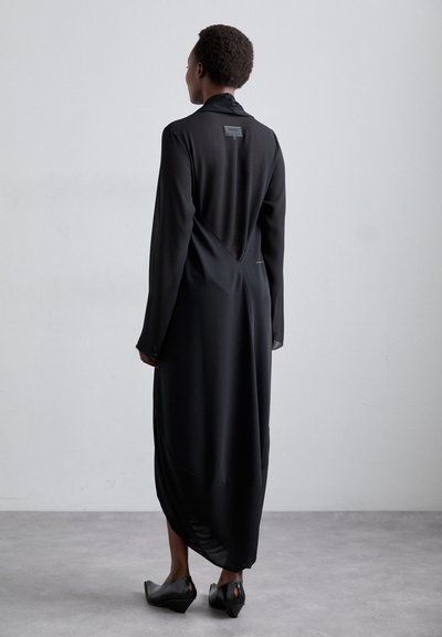 Black long-sleeve dress with a V-back cut, made of smooth fabric, featuring a high collar and seamless design. Black footwear completes the look.