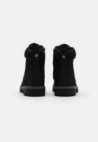 Bottines en suede noir avec une finition texturée, dotées d'une fermeture éclair et d'une sangle élastique à l'arrière, ainsi que d'une semelle rigide en caoutchouc avec des motifs.