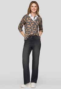 Beiger und grauer Pullover mit Muster und V-Ausschnitt über einem weißen Hemd mit Kragen, kombiniert mit dunklen Jeans und weißen Turnschuhen.