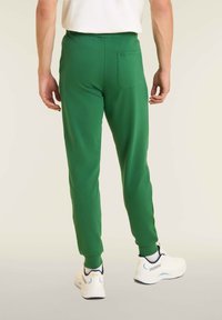 Pantaloni jogger verdi realizzati in un tessuto morbido con una vestibilità slim, dotati di una tasca posteriore e di una cintura elastica, abbinati a sneakers bianche.