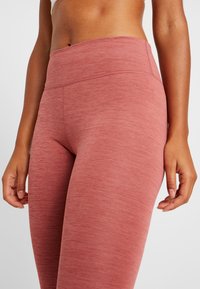 Leggings taille haute en tissu rose doux, texturé et sobre, avec une taille lisse et une silhouette ajustée.