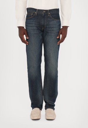Jeans de mezclilla azul oscuro con corte recto, ligero desgaste en la parte delantera y costuras a contraste. Combinados con mocasines de color claro.