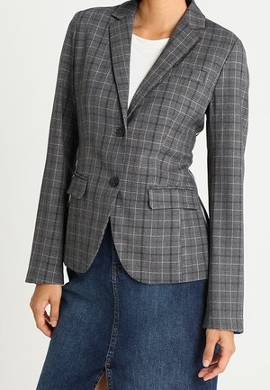 Blazer gris à carreaux ajusté avec deux boutons, revers crantés, poches à rabat, porté sur un top blanc et une jupe en jean bleue avec une fente à l'avant.