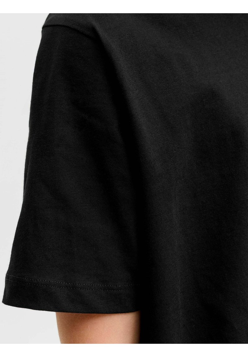 Μαύρο βαμβακερό T-shirt με κοντό μανίκι, εφαρμοστό στο πάνω μέρος του βραχίονα και στον ώμο, πάνω σε ουδέτερο φόντο.