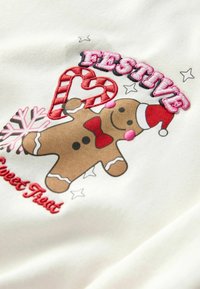 White fabric featuring a gingerbread man graphic with a red bow, Santa hat, candy cane, and the text "FESTIVE" in pink embroidery.