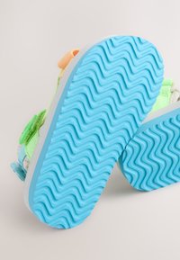 Scarpe per bambini con suola in gomma blu caratterizzata da un motivo a zigzag; tomaia in tela verde pastello, arancione e blu con cinturini in Velcro.