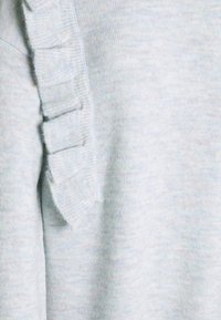 Suéter azul claro con una suave textura de punto, adornado con un detalle de volante vertical a lo largo de la costura lateral para añadir un interés visual.