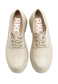 Beżowe skórzane buty o gładkiej fakturze, z okrągłym noskiem, sznurowanym zapięciem i gumową podeszwą. Wewnętrzna wyściółka ma na sobie białe litery "RKO".