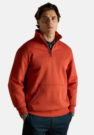 Orange sweatshirt with a quarter-zip collar, kangaroo pocket, ribbed cuffs, and a textured fabric. Paired with a navy checkered shirt underneath.