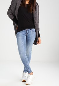 Cardigan grigio morbido, top nero fitted, jeans skinny azzurri chiari e sneaker bianche con dettagli marroni. Texture lisce e design casual.