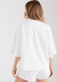 Biała, oversize'owa bluza z szerokimi rękawami, miękką fakturą i okrągłym dekoltem. Stylizowana z dopasowanymi białymi szortami.