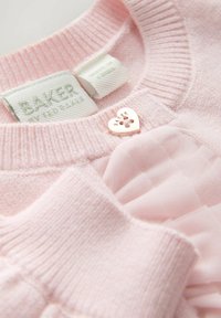 Gaismas rozā džemperis ar adītu ribveida tekstūru, tam ir sirds formas metāla poga. Iekļauta zīmola etiķete "BAKER by Ted Baker." Zemādas mīkstas auduma kārtas.