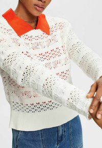 Strickpullover mit orangem Kragen, der offene Muster, Streifen mit unterschiedlichen Texturen und eine lockere Passform aufweist. Weiße Basis mit Farbakzenten.