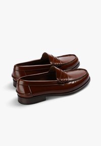 Mocasines de cuero marrón con un acabado brillante, que presentan un detalle de costura en la punta y un tacón bajo de un marrón oscuro.