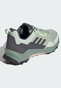Zapato deportivo Terrex con parte superior de malla en verde claro y gris, talón reforzado, suela negra robusta y cordones con patrón.