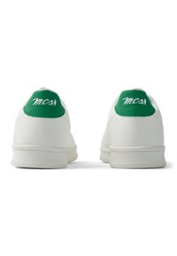 Zapatillas blancas con acabado de cuero suave, con talones acolchados en verde y el texto "MCS" en blanco en la parte trasera. Suelas de goma planas.
