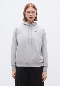 Hall halliga kapuutsiga dressipluus reguleeritavate nööridega ja väikese rohelise Lacoste'i logoga vasakul rinnal.