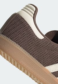Sneaker intrecciata marrone con un'accensione in pelle bianca, forma arrotondata, superficie texturizzata e suola in gomma traslucida con motivi antiscivolo.