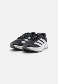 Des chaussures de sport noires avec une tige en maille, comportant trois rayures blanches, une languette rembourrée et une semelle blanche. Comprend des accents texturés au niveau du talon.