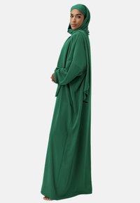 Grön abaya med långa ärmar, tillverkad av lätt tyg, med en draperad design och en matchande hijab. Enkel och elegant silhuett.