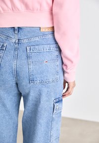 Lys blå denim bukser med løs passform, har to baklommer og en sidelomme, kombinert med en rosa ribb cuff genser.