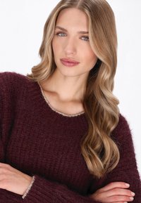 Burgundowa, dzianinowa bluza o luźnym kroju, z szerokim dekoltem i teksturowanym materiałem. Wykończona subtelnym, jasnym akcentem.