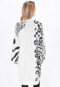 Maglione lungo e oversize bianco con accenti di stampa animale nera, caratterizzato da una texture morbida e pelosa e maniche larghe.