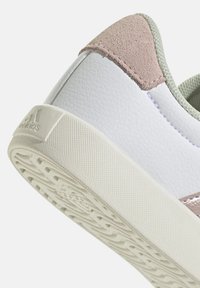 Baskets blanches avec des accents en suede rose, tige synthétique texturée et semelle en caoutchouc à motif. Logo Adidas embossé sur le talon.