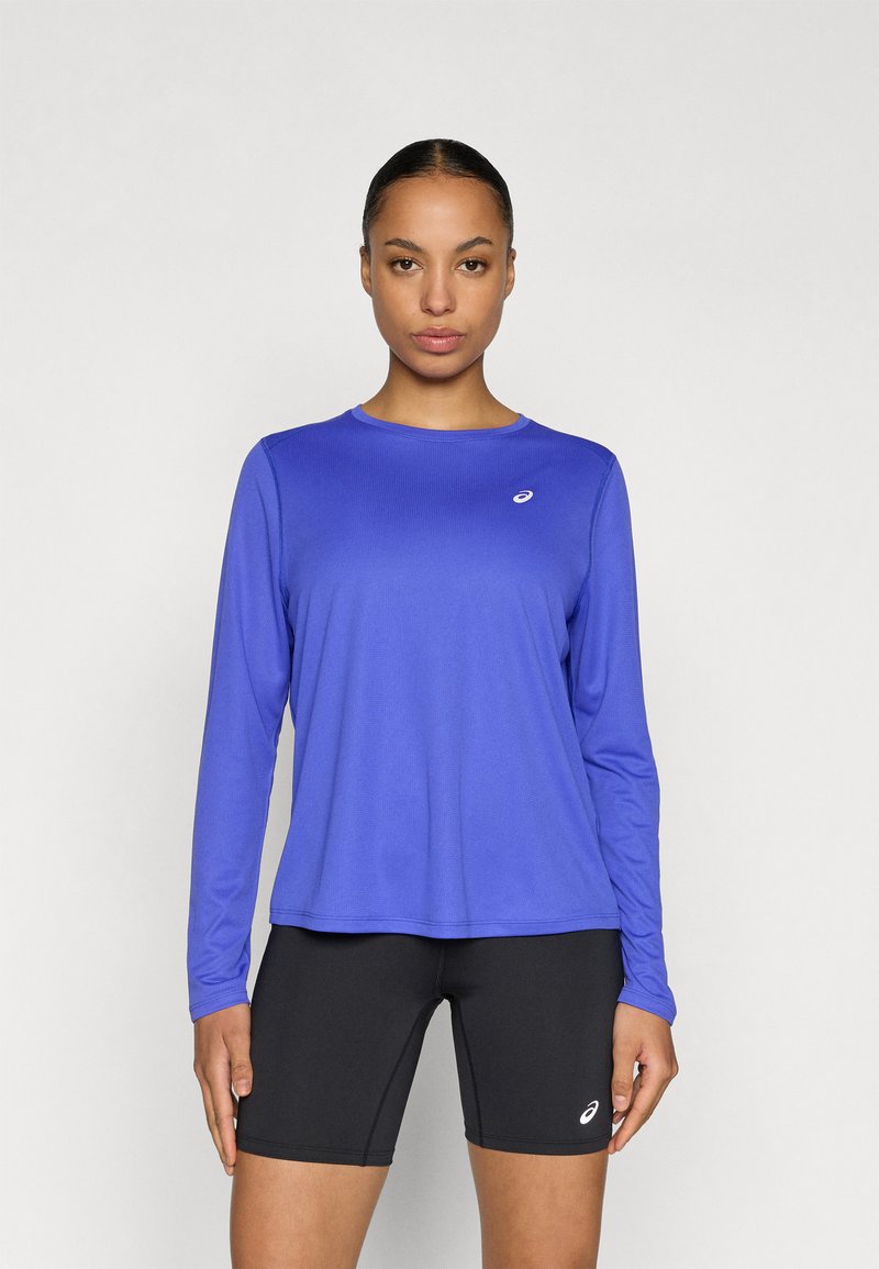 Αθλητική μπλούζα με μακριά μανίκια σε έντονο μπλε ύφασμα με ριμπ υφή· διαθέτει ένα μικρό λογότυπο στο στήθος και συνδυάζεται με μαύρο σορτς.