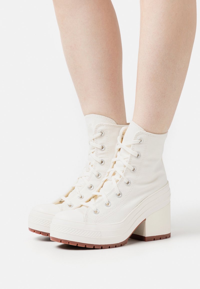 Witte hoge sneakers met een bovenwerk van canvas, een ronde neus, een robuuste witte plateauhak en een rubberen zool met textuur aan de zijkant en een vetersluiting.