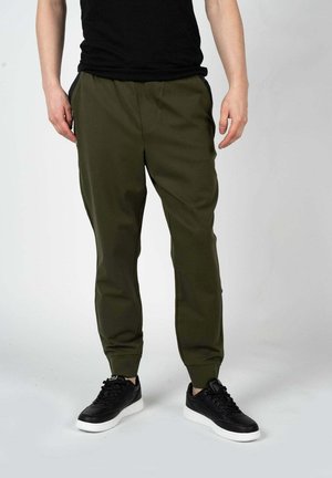 Pantalones jogger de color verde oliva hechos de tejido suave, con puños elásticos y bolsillos laterales, combinados con zapatillas negras.