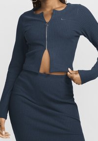 Marineblaues, geripptes Strick-Crop-Top mit langen Ärmeln, ausgestattet mit einem Reißverschluss und einem runden Halsausschnitt, kombiniert mit einem passenden Rock in hoher Taille.