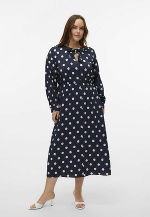 Navy polka dot dress with a bow tie neck, long sleeves, gathered waistband, and midi length. Made from a textured, lightweight fabric.