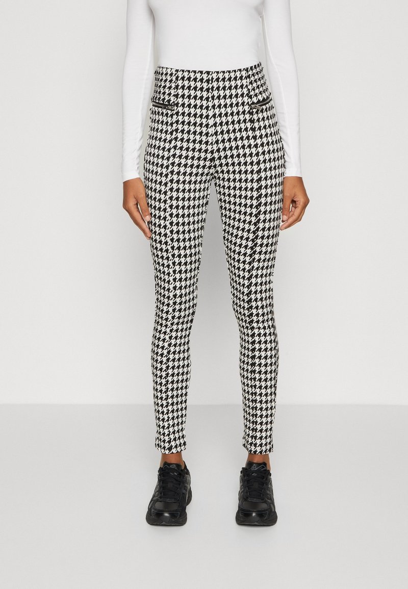 Broek in zwart-wit houndstooth patroon, slimfit ontwerp met zijzakken, gecombineerd met zwarte sneakers. Gladde stoftextuur.