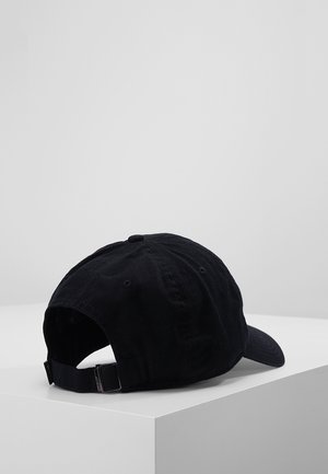 Casquette de baseball noire réglable avec boucle métallique à l'arrière, affichée sur une surface blanche en coin sur un fond gris clair uni.