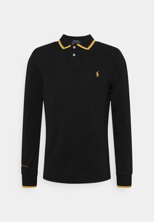 Zwart poloshirt met lange mouwen, met gele accenten op de kraag en mouwen. Voorzien van een knoopsluiting met twee knopen en een klein geel logo op de borst.
