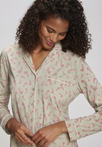 Lys grønn pysjamasgenser med rødt kanelstangmønster, lange ermer, knappelukking foran og brystlomme. Mykt stoff med avslappet passform.