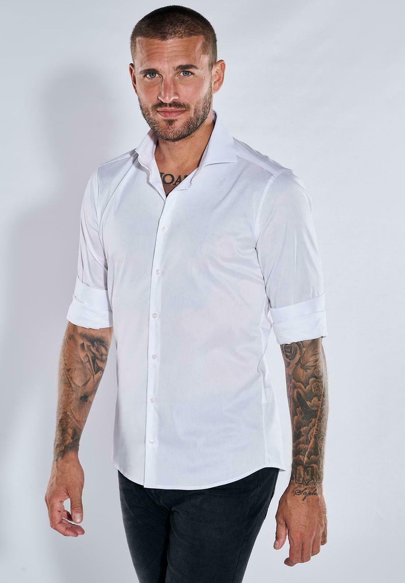 Weißes, kurzärmliges Hemd mit umgeschlagenen Ärmeln, aus einem glatten Stoff gefertigt. Verfügt über einen klassischen Kragen und einen dezenten Glanz. Getragen mit dunklen Jeans.