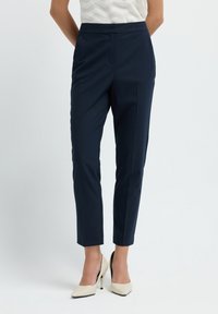 Laadun mukaiset meripinnalle raidoitetut housut, joissa on muotoiltu istuvuus, kapenevat lahkeet ja tasainen etuosa, yhdistettynä vaaleanbeigeihin korkokenkiin.