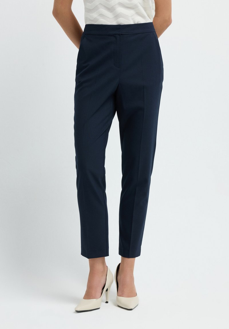 Laadun mukaiset meripinnalle raidoitetut housut, joissa on muotoiltu istuvuus, kapenevat lahkeet ja tasainen etuosa, yhdistettynä vaaleanbeigeihin korkokenkiin.