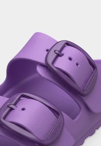 Μωβ σανδάλι Birkenstock με δύο ρυθμιζόμενους ιμάντες με αγκράφες, υφή στο πέλμα και καμπυλωτή σόλα, σε κοντινό πλάνο σε λευκό φόντο.