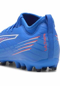 Scarpa da calcio blu con tomaia testurizzata, righe a contrasto arancioni e collo imbottito con linguetta sul retro. Suola nera con tacchetti.