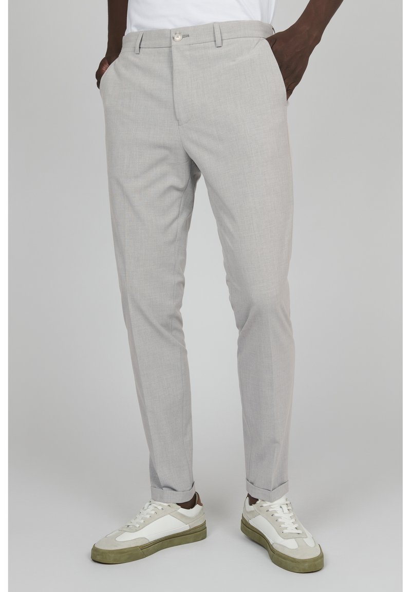 Pantalones ajustados de color gris claro, confeccionados en tejido texturizado, con frente plano, bolsillos laterales y diseño ajustado. Combinados con zapatillas blancas y verdes.