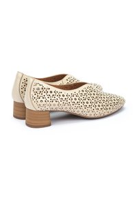 Chaussures en cuir perforé beige avec un bout rond et un petit talon en bois empilé. Présentent des découpes florales et une doublure intérieure lisse.